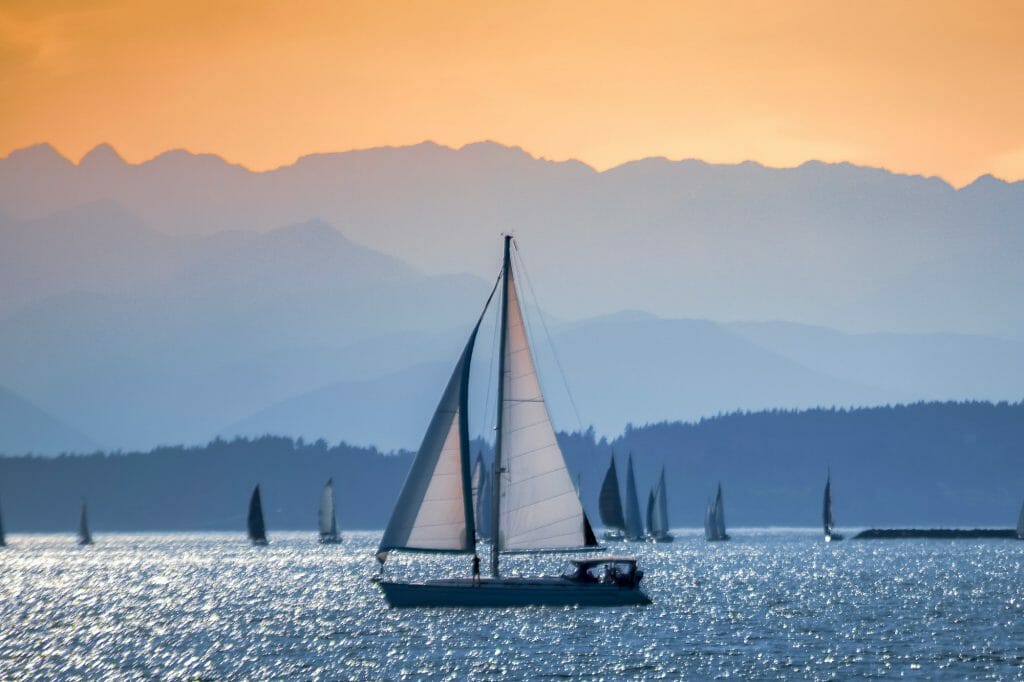 Golden hour sunset with mountain peaks and sailboat sails.